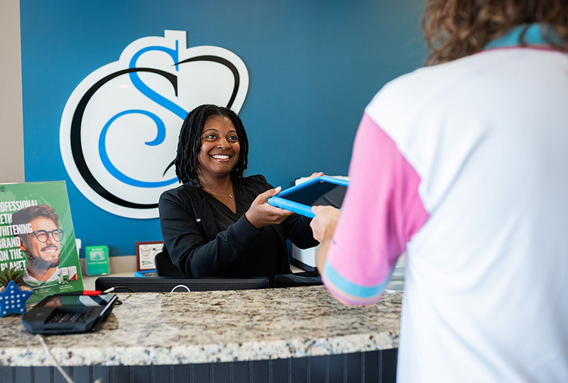 The image shows a person standing behind a desk with a sign that reads  Sport Clips  on it, interacting with another individual who appears to be receiving a service at the counter.