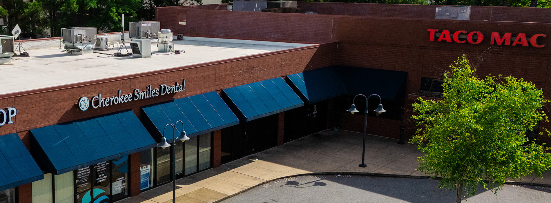 The image shows a view of a restaurant with an outdoor seating area, featuring a Taco Mac sign and a tree in front of the building.