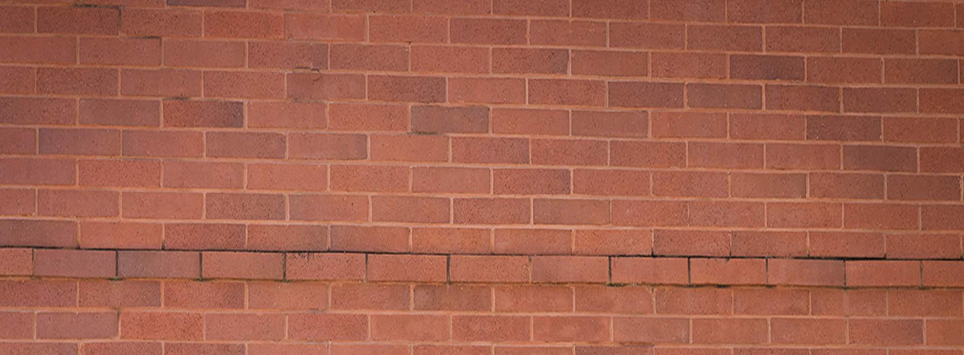 The image shows a red brick wall with a single rectangular opening on its right side, set against a gray background.