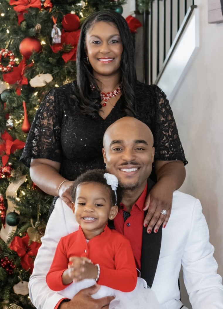 A family posing together in front of a Christmas tree with red ornaments and lights.