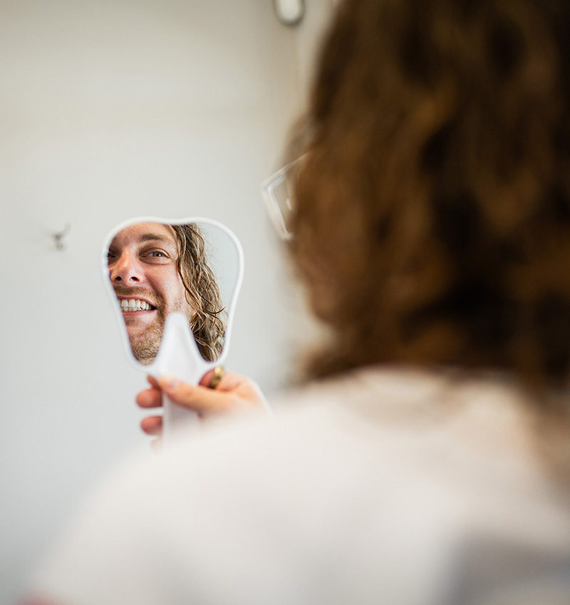 The image shows a person applying makeup to their face while looking into a mirror, using a magnifying mirror to ensure precision.