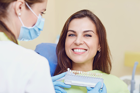 A woman sitting in a dental chair receiving a dental check-up from a dentist, with both smiling at the camera.