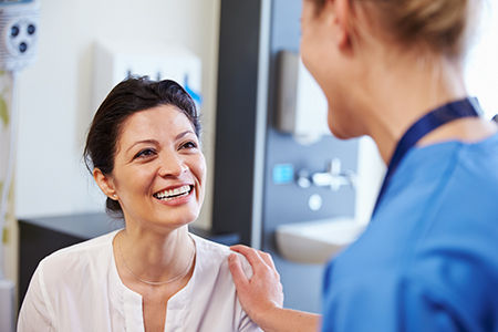 An image featuring two women in a medical setting  one appears to be a patient receiving care from a healthcare professional who seems to be a nurse or doctor, with both smiling and engaged in conversation.