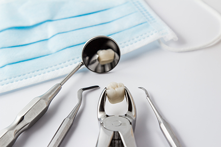 The image shows a collection of dental tools, including a pair of tweezers with a tooth in them, placed on a blue cloth with a white background.