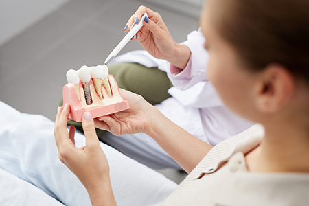 Woman holding a fake tooth in her hand while sitting in a dental chair.